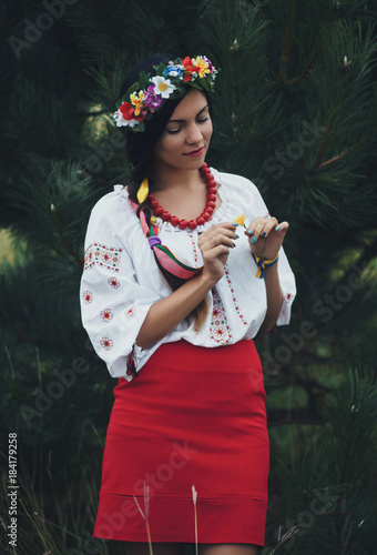 Beautiful woman in colorful ukrainian traditional dress holding herself and enjoying summer in green forest photo