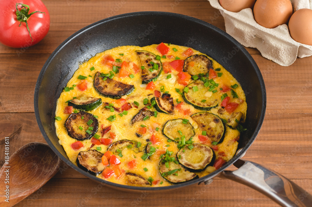 Omelette with zucchini, red paprika and chives. Frittata in frying pan on wooden board. Omelette with zucchini, red paprika and chives. Frittata in frying pan on wooden board.