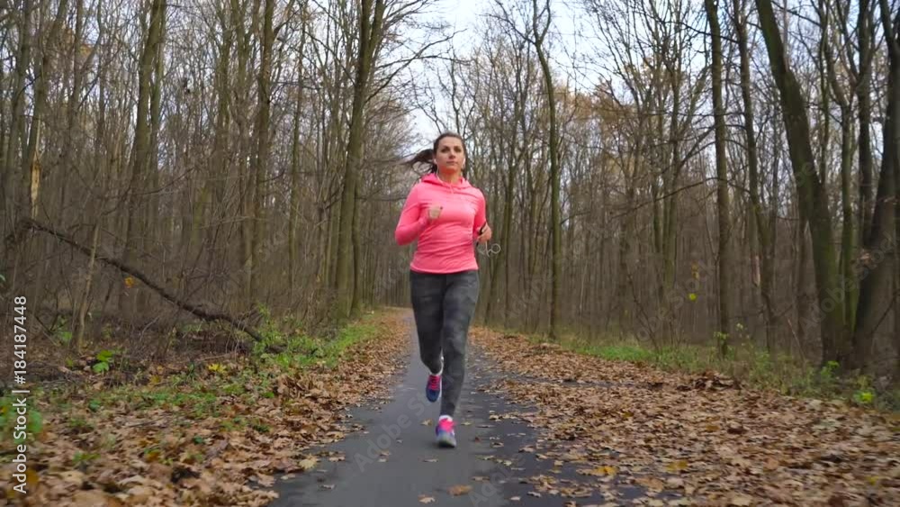 Close up of woman with headphones and smartphone running through an autumn forest at sunset Close up of woman with headphones and smartphone running through an autumn forest at sunset