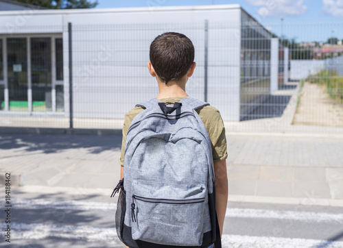 Teenage school boy with a backpack on his back walking to school