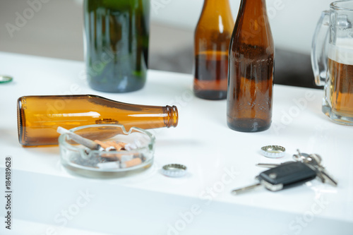 Beer bottles, ashtray and keys on white surface