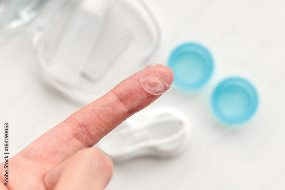 Contact lens on finger on the background of container for storage of lenses Contact lens on finger on the background of container for storage of lenses