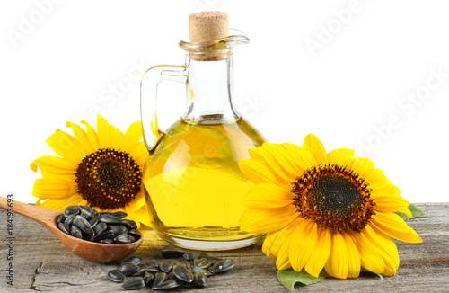 Sunflower oil in glass jug , seeds and flower on old wooden table with white background