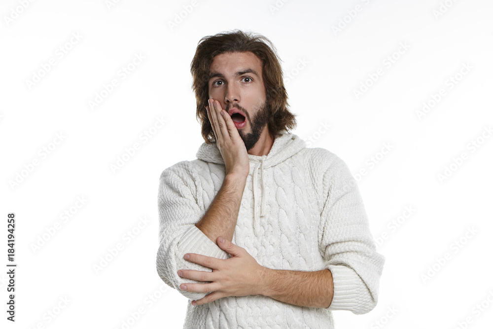 Studio shot of astonished bug eyed young European male with fuzzy beard and wavy hair opening mouth in surprise, shocked with unexpected news, being lost for words, holding hand on his cheek Studio shot of astonished bug eyed young European male with fuzzy beard and wavy hair opening mouth in surprise, shocked with unexpected news, being lost for words, holding hand on his cheek