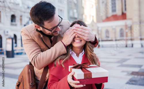 Surprise for girlfriend. Man keeps his girlfriend eyes covered while she holding a gift. Dating, love and tenderness, lifestyle concept photo