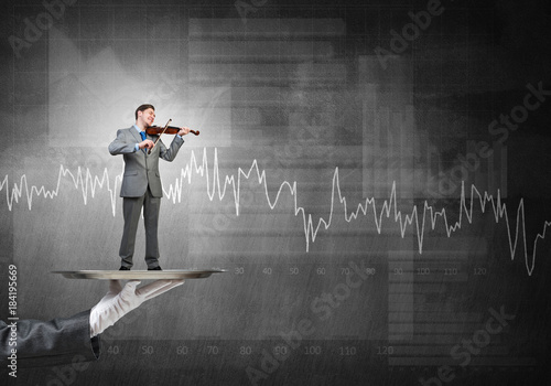 Businessman on metal tray playing violin against graphs and diagrams background