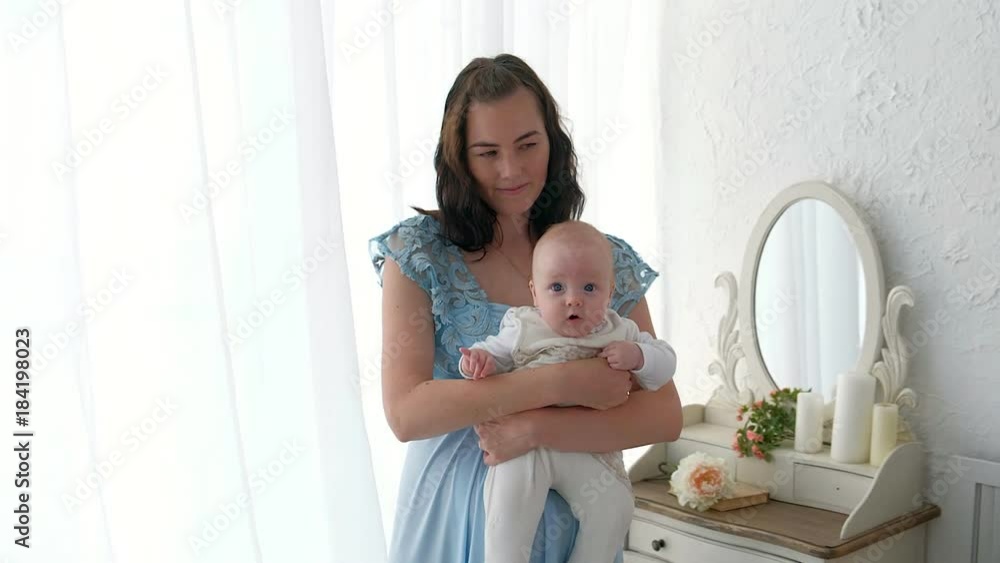 Tracking mother putting baby to sleep while walking . Attractive woman holding baby in hands and walk across living room with bright window curtains in background. Tracking mother putting baby to sleep while walking . Attractive woman holding baby in hands and walk across living room with bright window curtains in background.