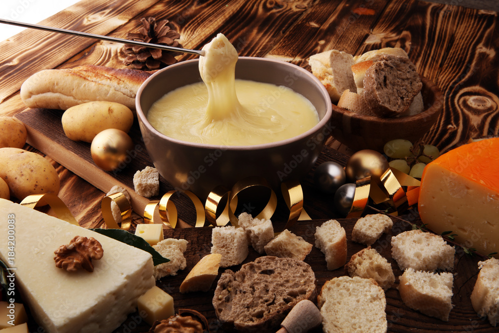 Gourmet Swiss fondue dinner on a winter evening with assorted cheeses on a board alongside a heated pot of cheese fondue with two forks dipping bread and white wine behind in a tavern or restaurant. Gourmet Swiss fondue dinner on a winter evening with assorted cheeses on a board alongside a heated pot of cheese fondue with two forks dipping bread and white wine behind in a tavern or restaurant.