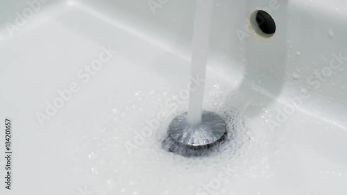 Home water faucet drain closeup with water flow dropping in from the faucet