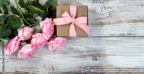 Six pink roses and gift on rustic white wooden background