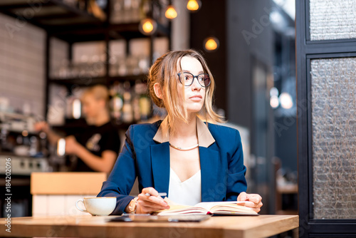 Young businesswoman strictly dressed in suit working with notebook at the modern cafe interior