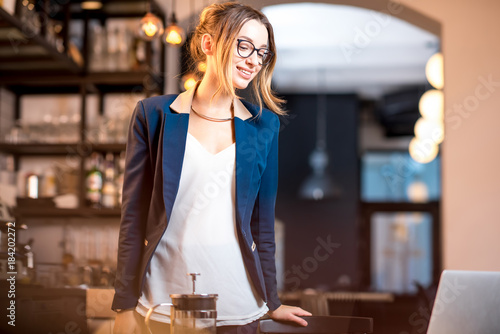 Young businesswoman strictly dressed in the suit coming with bag at the cafe table having a coffee break