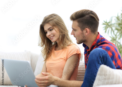 young couple sitting on sofa and looking at pictures on the laptop.