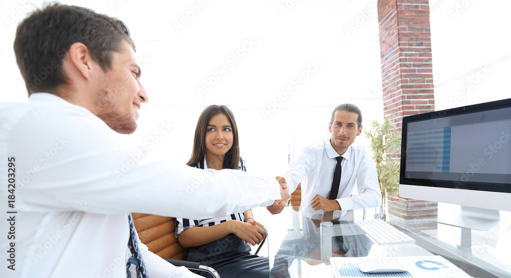 Fototapeta premium men shaking hands and smiling while sitting at the desk