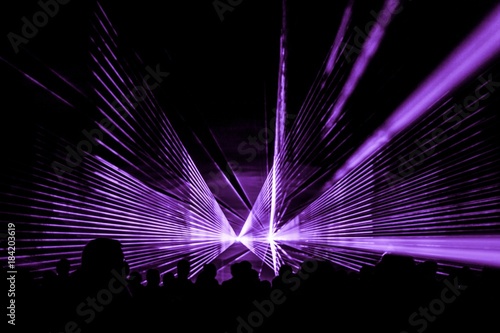 Purple laser show nightlife club stage with party people crowd. Luxury entertainment with audience silhouettes in nightclub event, festival or New Year's Eve. Beams and rays shining colorful lights