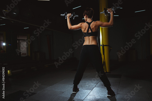 fitness girl doing crossfit exercises in gym with dumbels in dark hall, sporty woman sexy in pose doing functional training, poster banner healthy lifestyle photo