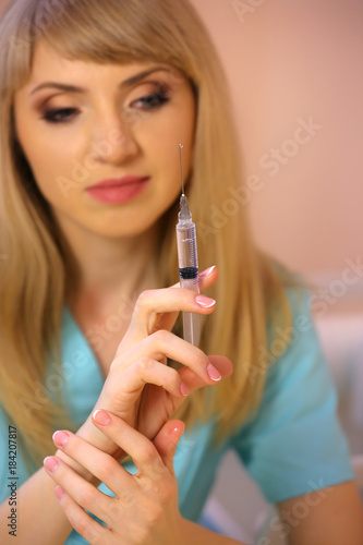 Beautiful nurse with a syringe. Portrait of young female doctor smiling with syringe in hand.
