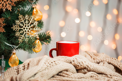 A Christmas tree decorated snowflakes and a garland, cup of coffee with knitted scarf on the background of a bokeh and white boards. Merry Christmas, ideas for postcards for winter holidays