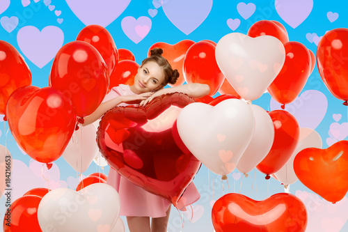 Beautiful girl with balloons in the shape of hearts, flies into the sky. Fantasy on the theme of Valentine's Day. Woman model in vanilla pink dress in love.