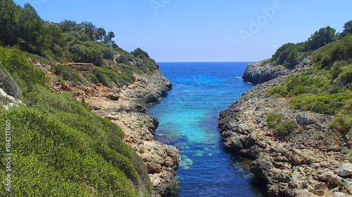 A blue river flows between the rocks and green trees on the coast of Majorca in the Mediterranean Sea