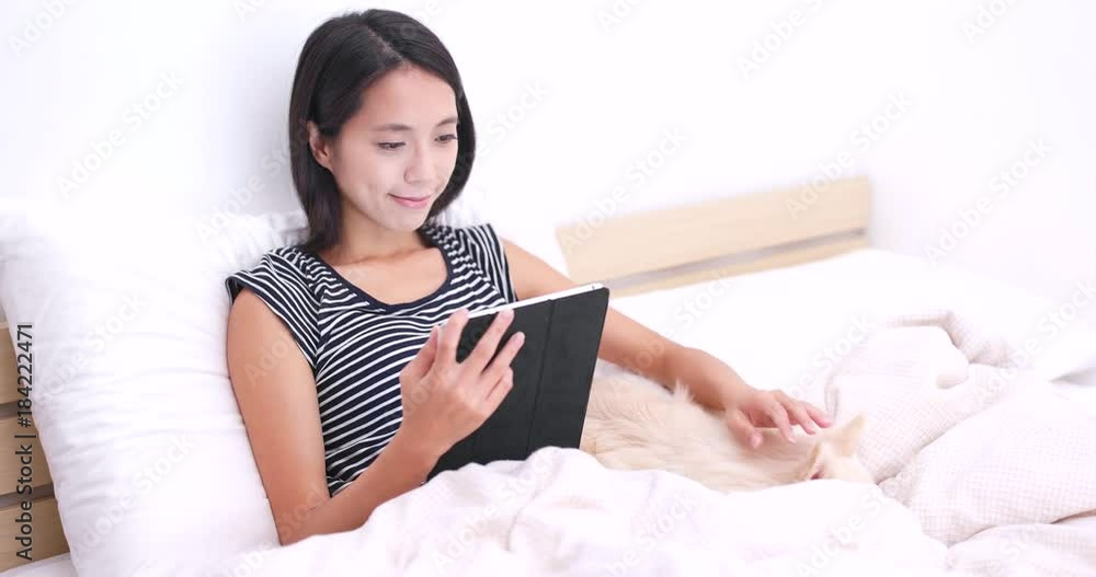 Woman watching on digital tablet and lying on bed with her dog Woman watching on digital tablet and lying on bed with her dog