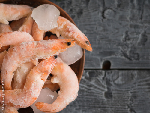 Frozen prawns in an earthenware bowl on a rustic wooden table. Top view.