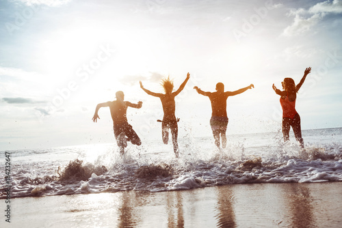 Four happy friends runs to sunset beach