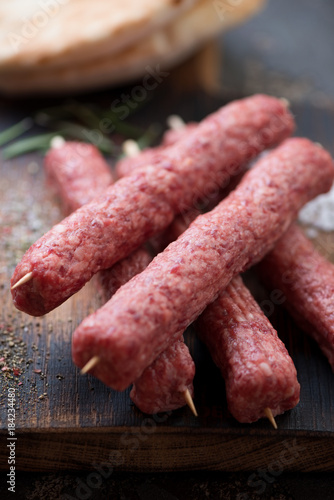 Close-up of raw balkan cevapi or cevapcici sausages on wooden skewers, shallow depth of field, selective focus