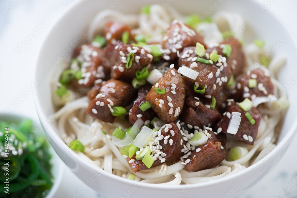 Close-up of udon noodles with pork meat in honey sauce, green onion and sesame seeds, selective focus, shallow depth of field Close-up of udon noodles with pork meat in honey sauce, green onion and sesame seeds, selective focus, shallow depth of field