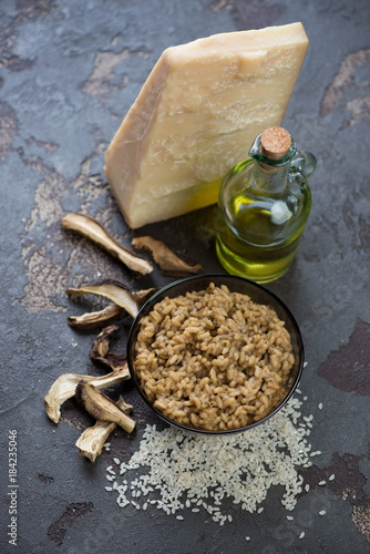 Risotto with cep boletus and some of its cooking components over brown stone background, studio shot