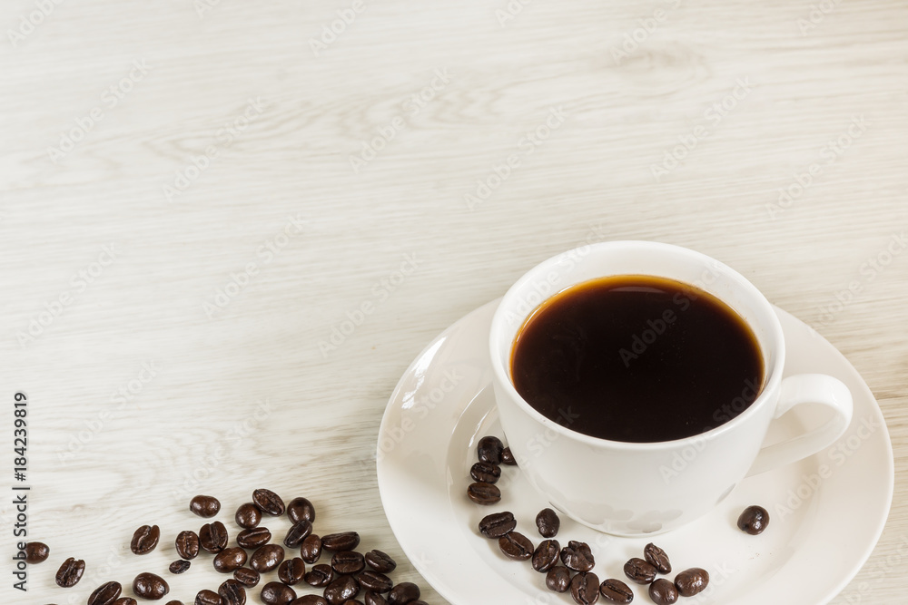 Black coffee in white cup and coffee beans on soft wooden background.