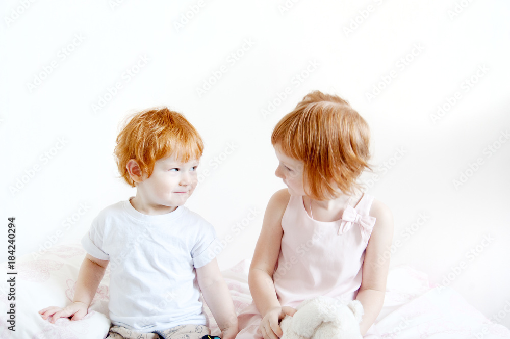Red-haired brother and sister are sitting on the bed Red-haired brother and sister are sitting on the bed