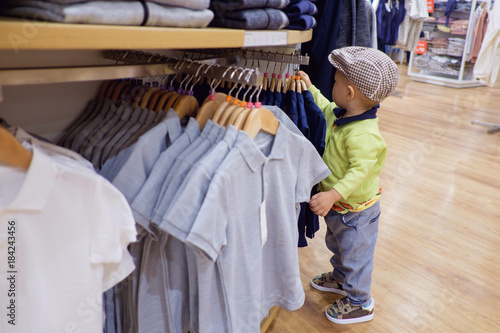 Cute little Asian 18 months / 1 year old toddler baby boy child choosing & buying kids clothes in garments shop,