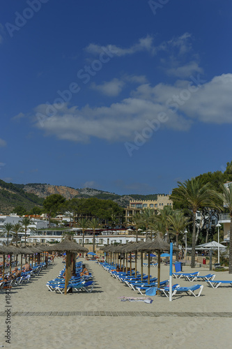the view of the sun loungers and parasols on the sandy beach on background of mountains and blue sky © westermak15