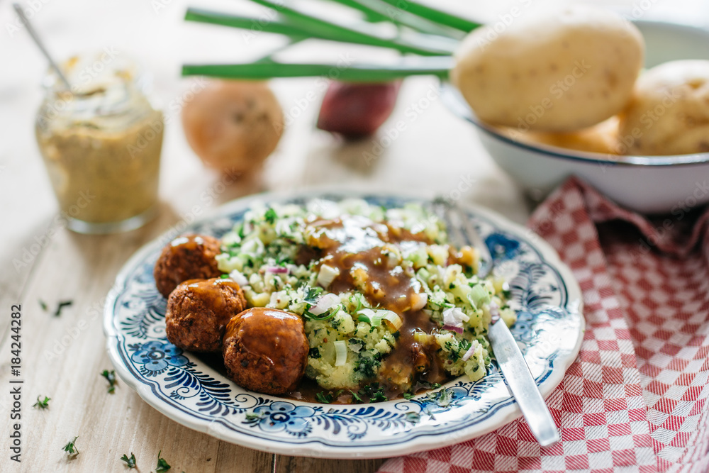 Typical Dutch dish: mashed potatoes with kale, vegan meatballs with gravy, blue plate, nice soft bokeh background, with props Typical Dutch dish: mashed potatoes with kale, vegan meatballs with gravy, blue plate, nice soft bokeh background, with props