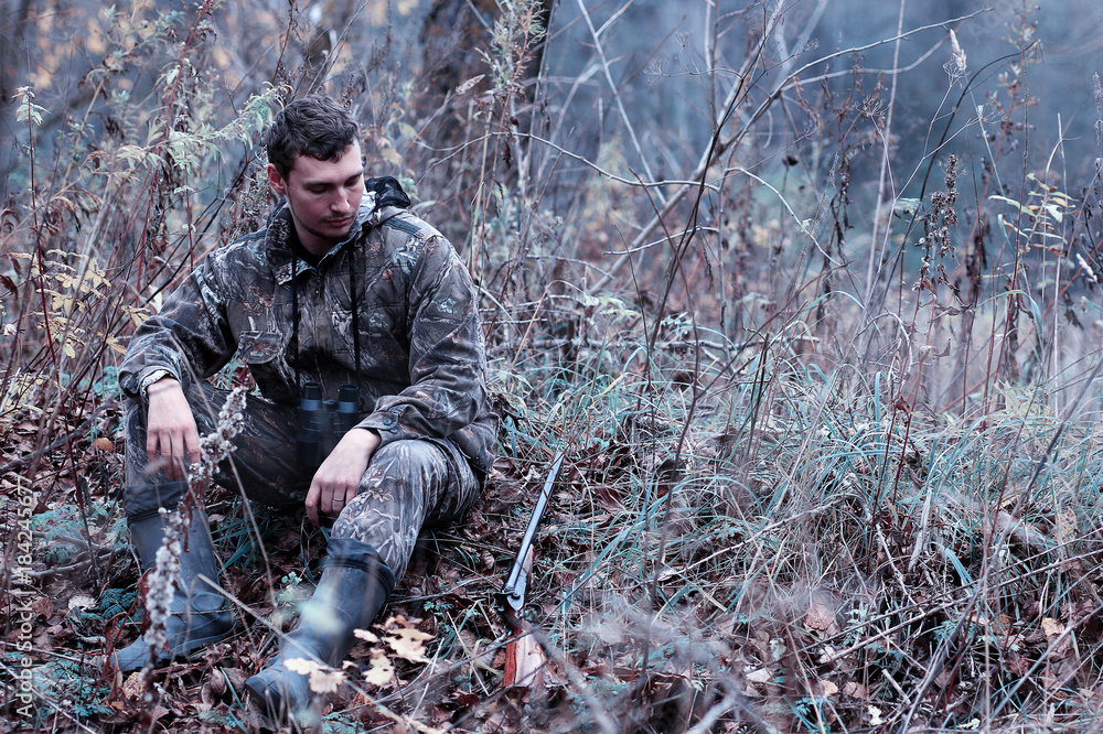 A man in camouflage and with a hunting rifle in a forest on a sp