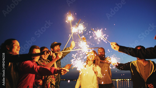 Group of young friends having a beach party. Friends dancing and celebrating with sparklers in twilight sunset photo