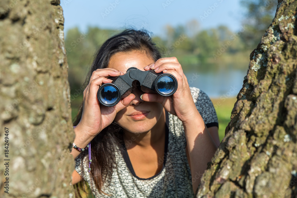 Woman looking through binoculars near trees Woman looking through binoculars near trees