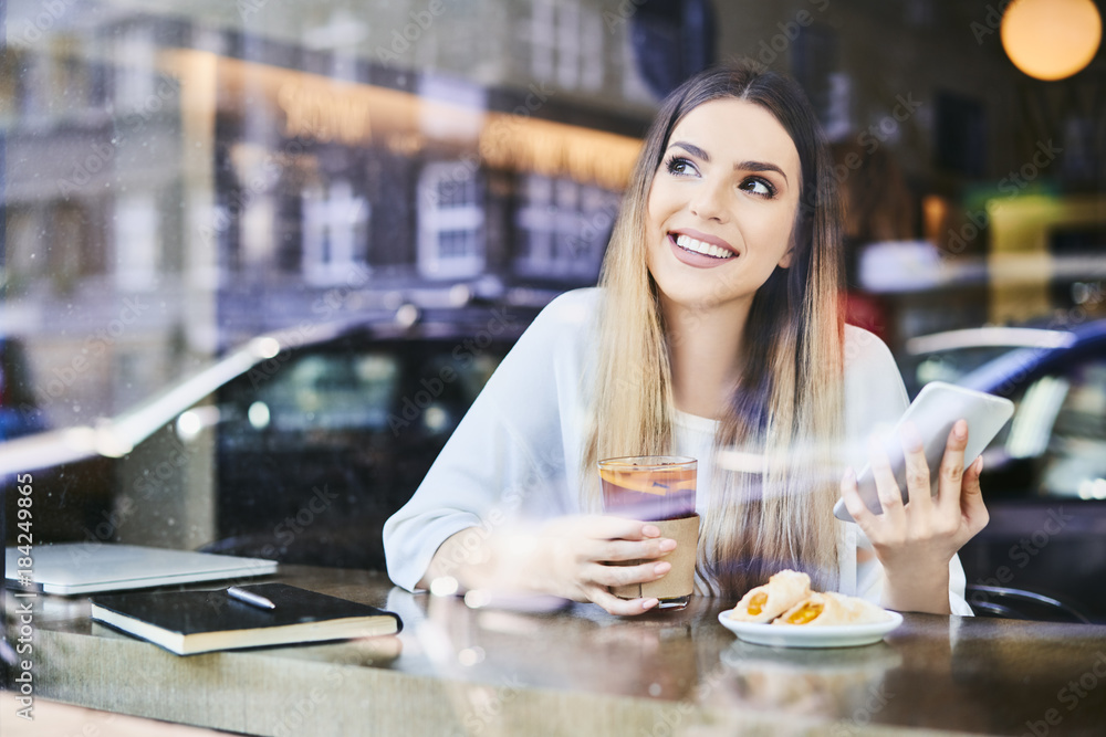 Beauitful smiling woman using phone having drink and dessert in cafeteria
