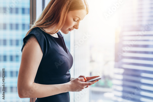 Pretty smilingwoman using smartphone standing in office
