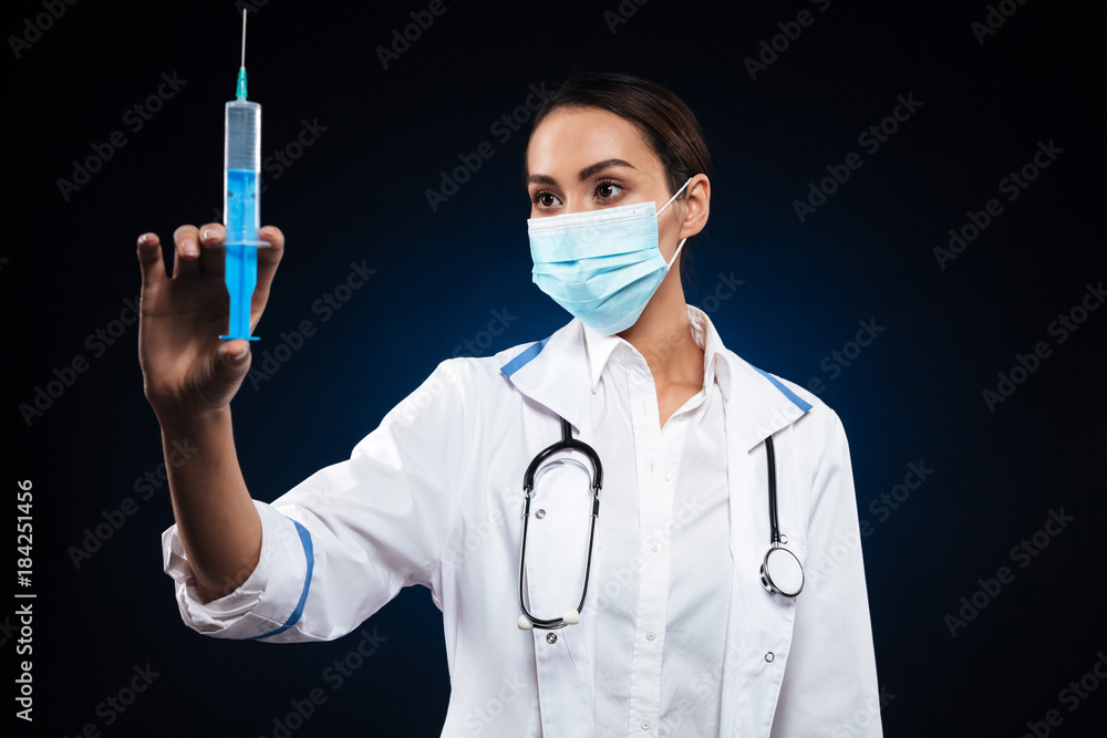 Young serious lady in medical mask holding and looking at syringe Young serious lady in medical mask holding and looking at syringe