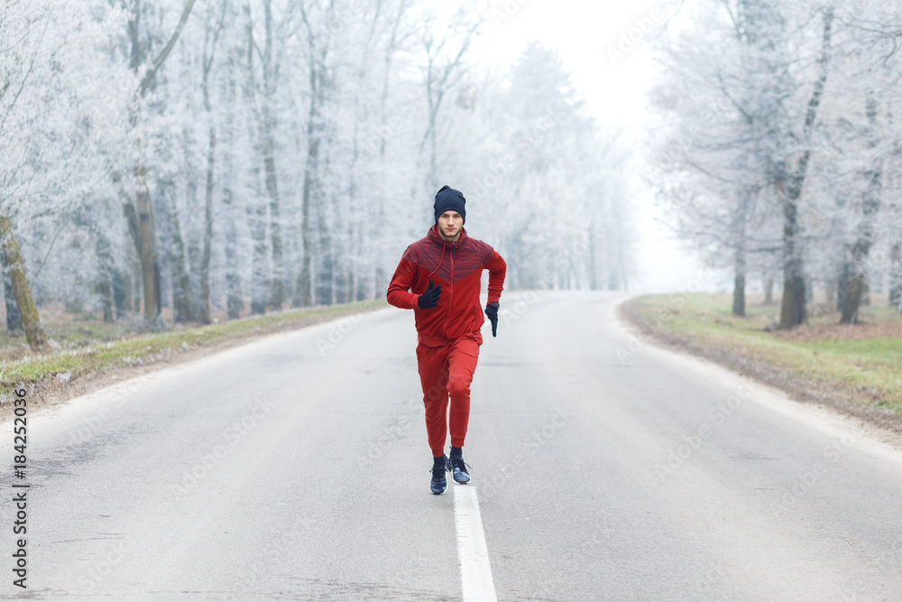 Young man running on a cold winter day on a road.