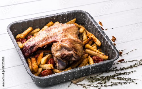 Fried turkey wing in baking tray with herbs on white wooden table