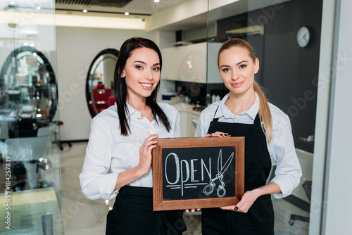 beautiful hairdressers standing with signboard open photo