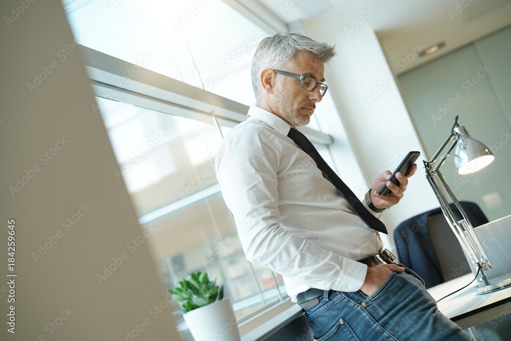 Businessman in office sending messages with smartphone Businessman in office sending messages with smartphone