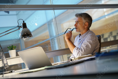Businessman in office being thoughtful in front of laptop photo