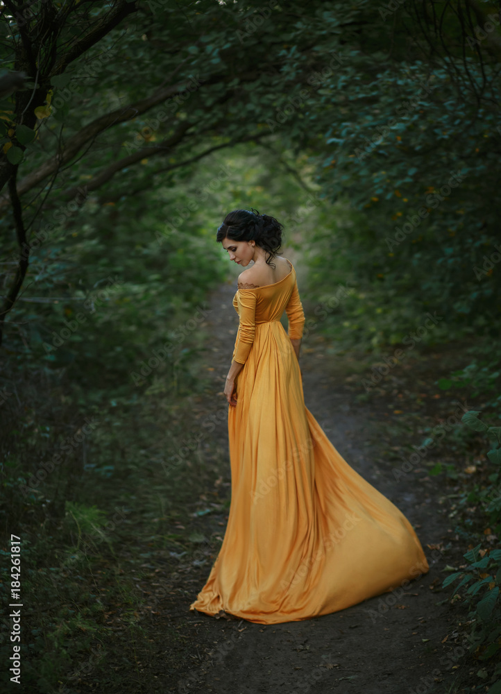 A fragile, tender girl in a yellow vintage dress . Background of a mystical arch of green trees. Artistic Photography