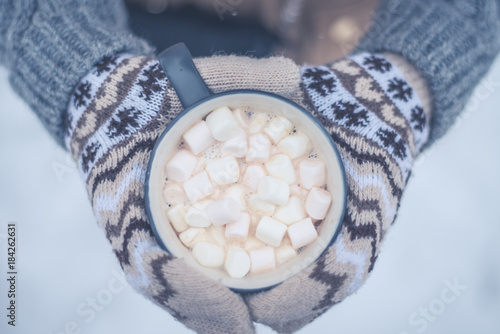 hands of the girl holding a mug with hot chocolate on the background of snow