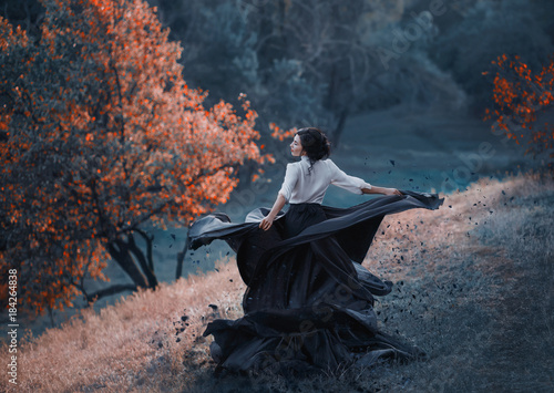 A girl in a vintage dress splits into particles, like ash. Background wild nature. Artistic Photography