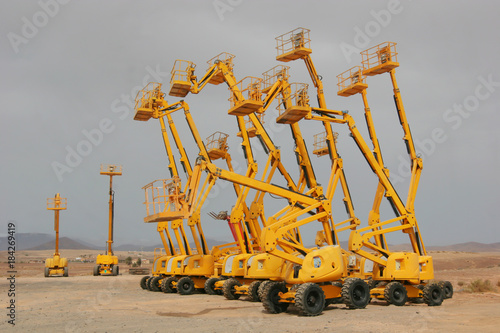 Several colorful self propelled wheeled hydraulic articulated boom lifts with telescoping boom and yellow basket on a desert landscape background
